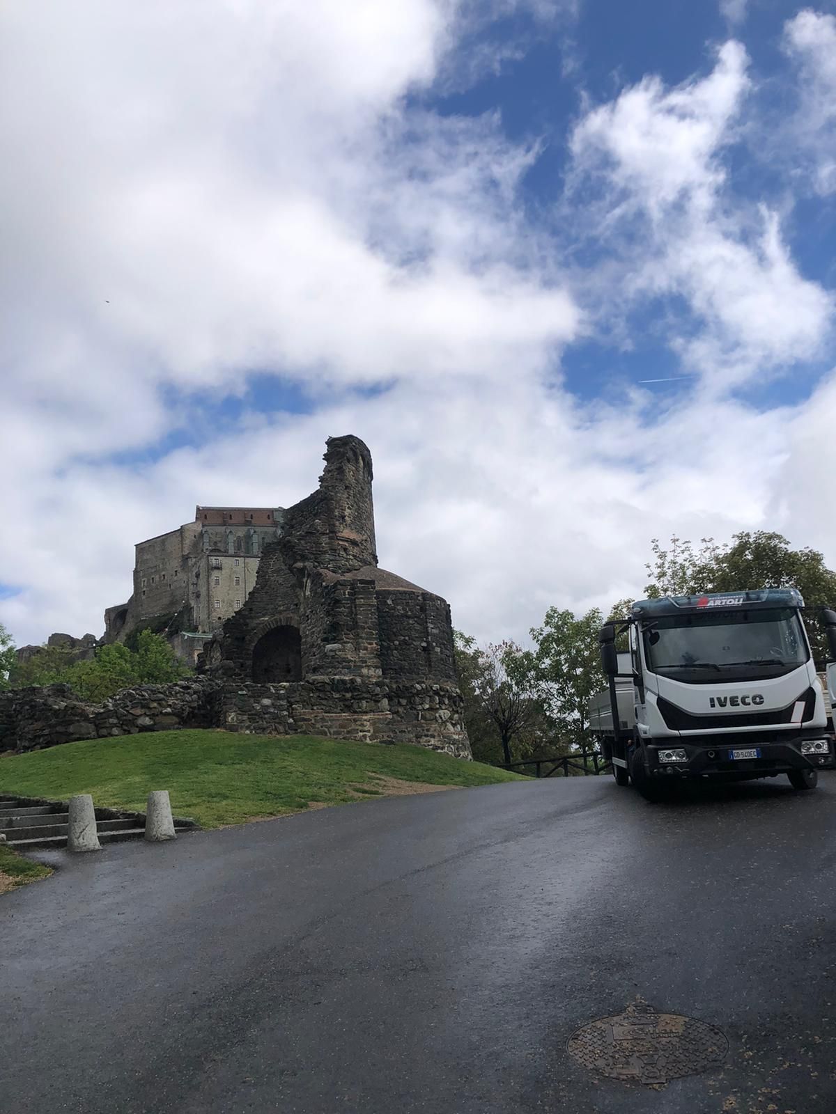 Camion da cantiere che solleva una struttura in acciaio accanto a una casa in ristrutturazione, con un pannello laterale personalizzato con il logo aziendale.