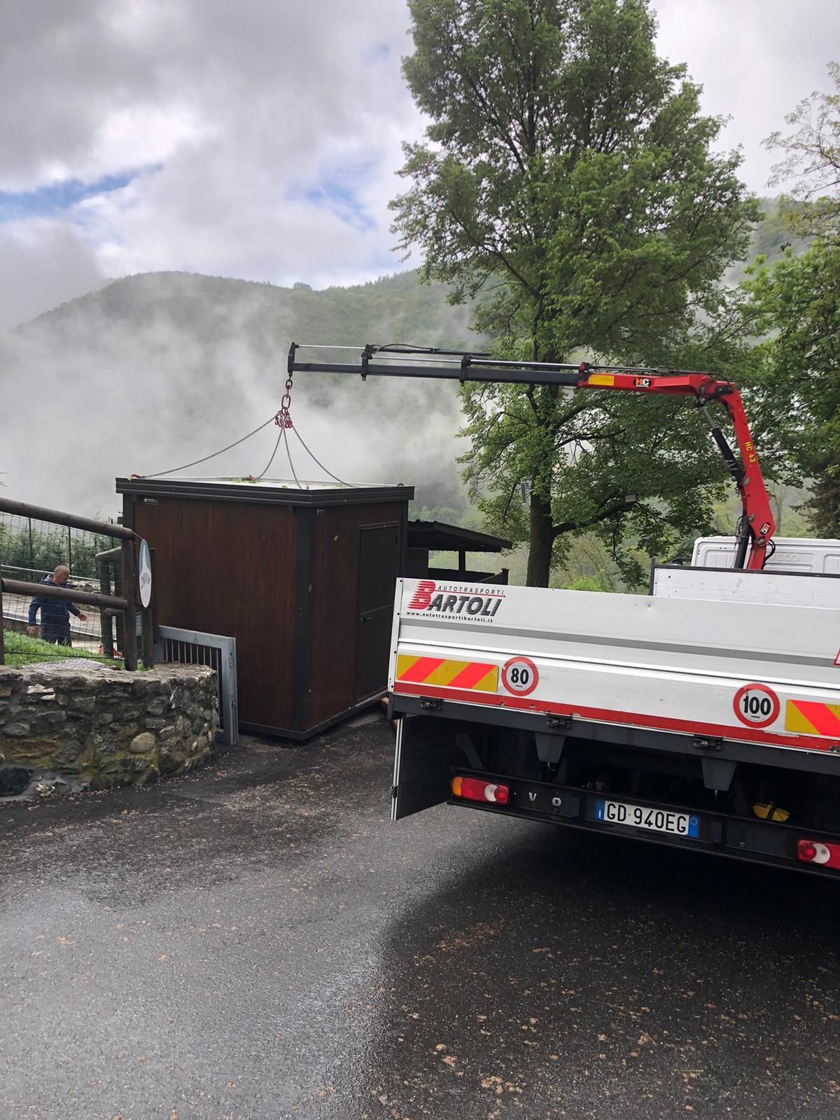 Una gru solleva fasci di mattoni sopra una casa in un soleggiato cortile residenziale.