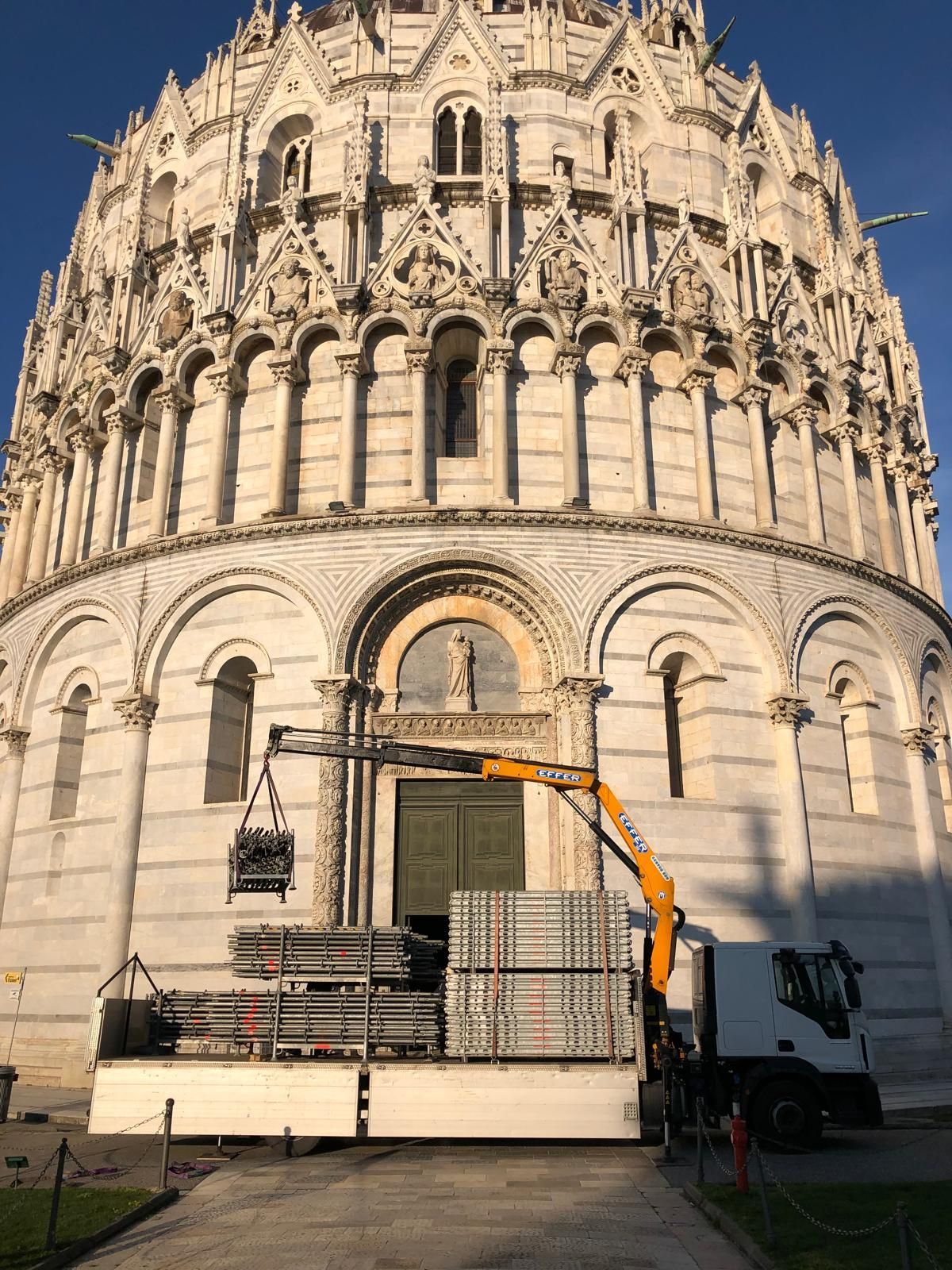 Piattaforma di manutenzione con gru di fronte a una facciata bianca e riccamente decorata di una cattedrale, immersa nella calda luce del sole.
