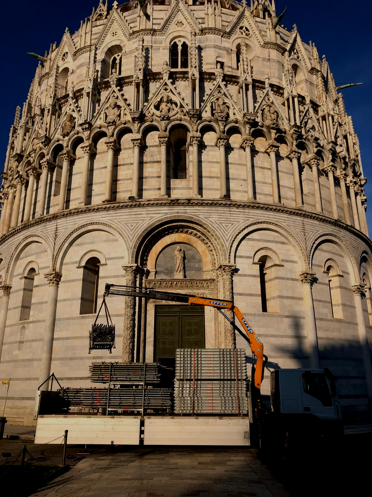Piattaforma di manutenzione con gru di fronte a una facciata bianca e riccamente decorata di una cattedrale, immersa nella calda luce del sole.