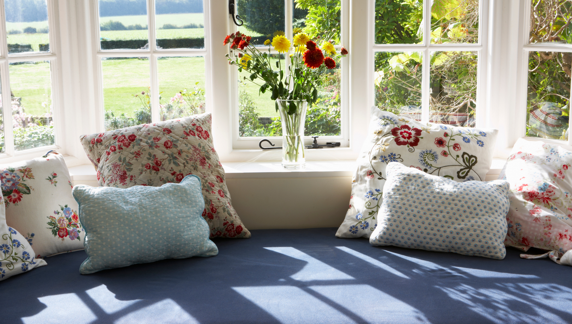 A window seat with pillows and a vase of flowers