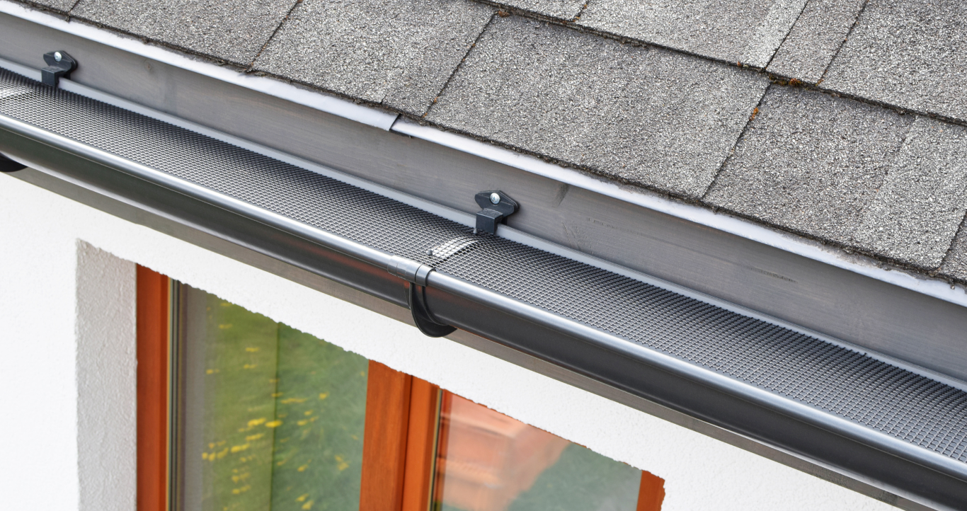 A close up of a gutter on a roof next to a window.
