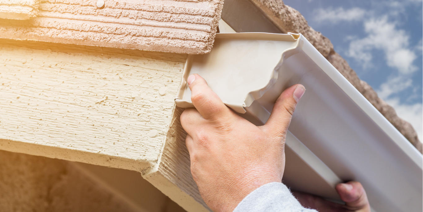A person is installing a gutter on the side of a house.