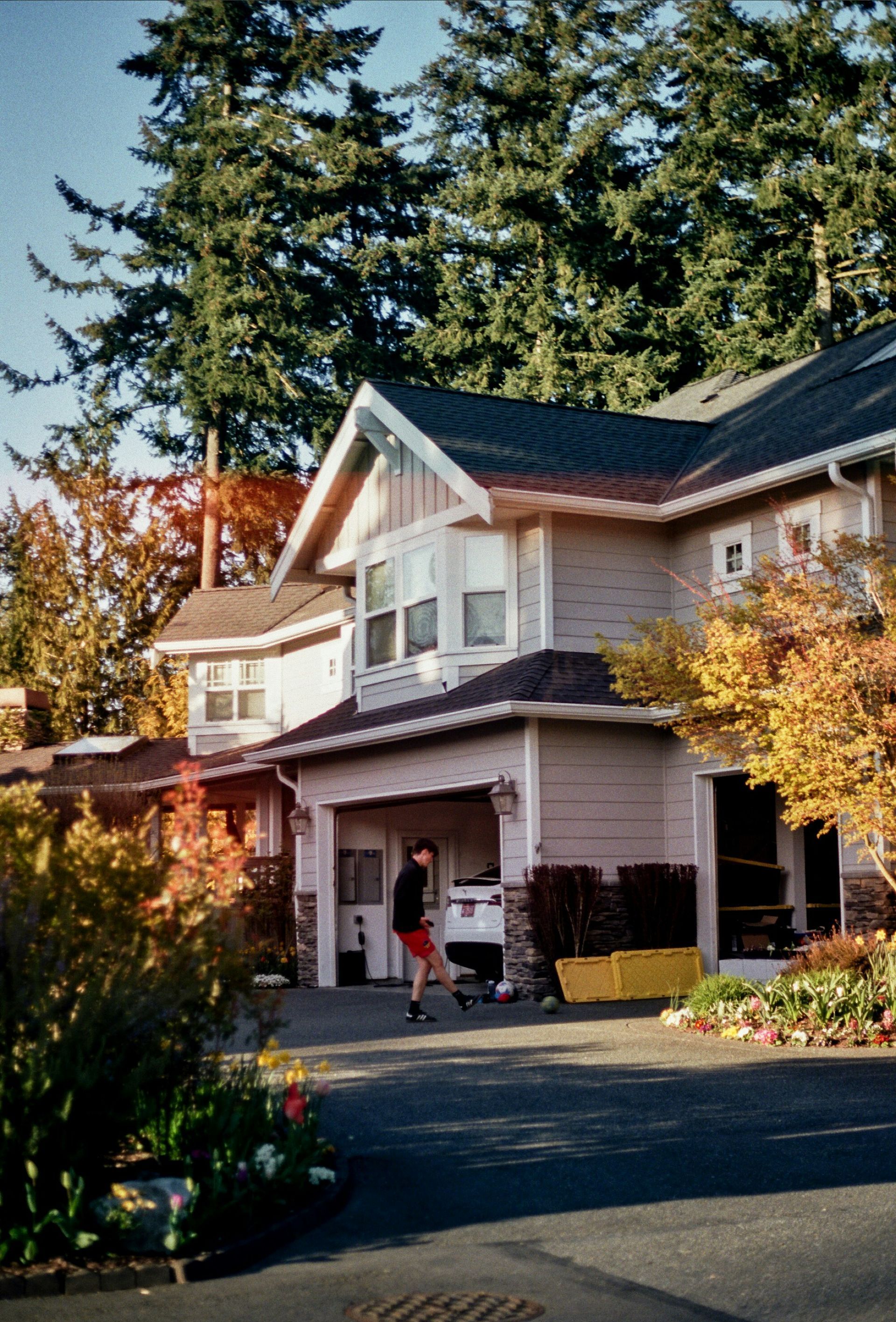 A man is walking in front of a house with a black roof