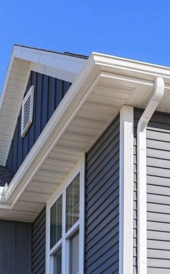 A gray house with a white gutter and a blue sky in the background.
