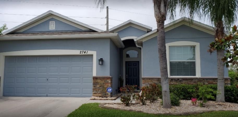 A blue house with a garage and a palm tree in front of it.