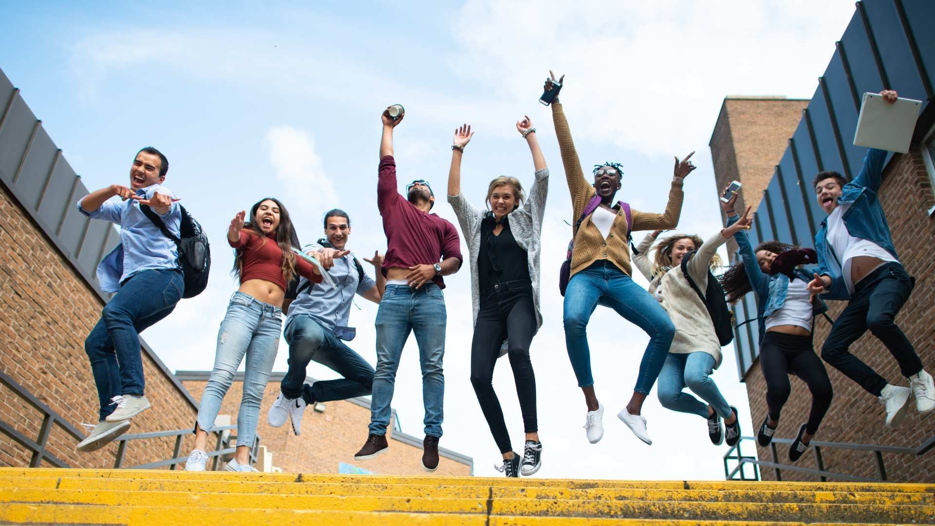 Group of friends jumping and cheering on yellow steps between brick buildings