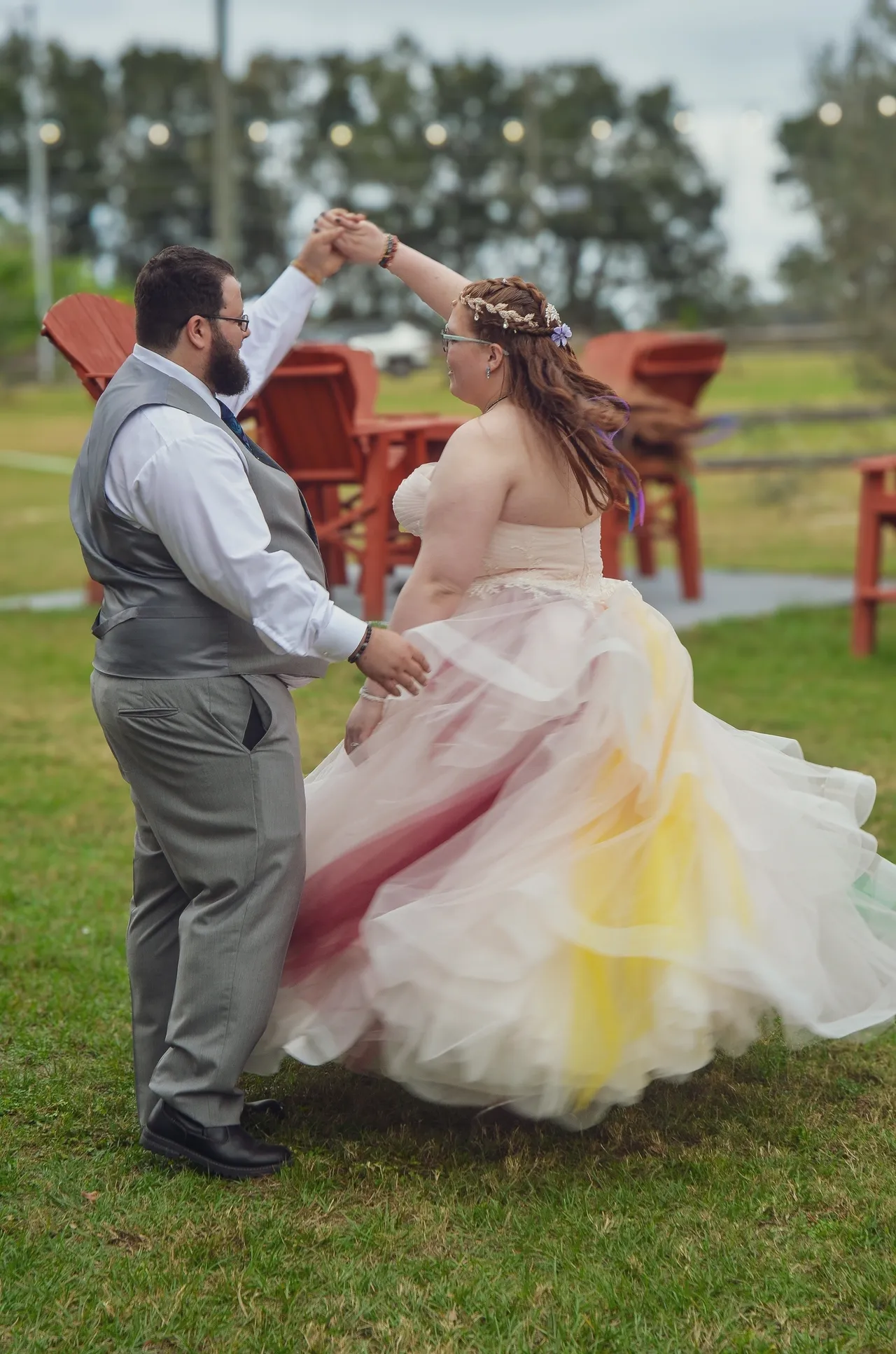 A couple dances outdoors in a field; the person in a colorful, flowing ballgown twirls while the other leads them.