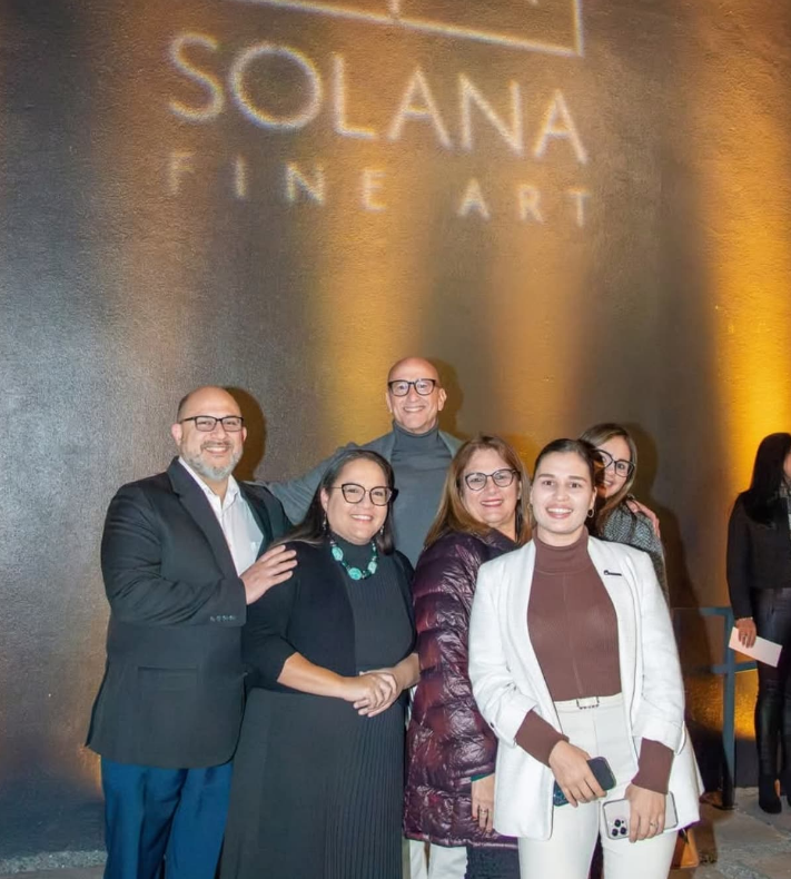 A group of six people stand smiling in front of a wall with a projected 
