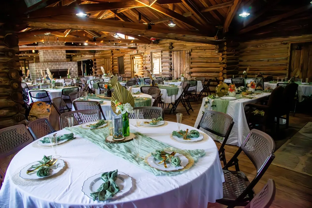 A rustic lodge interior set for an event with round tables featuring white tablecloths, sage runners, and place settings.