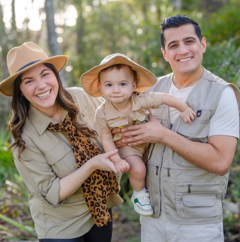 A family wearing khaki safari-themed clothing and hats poses in a park, smiling at the camera.