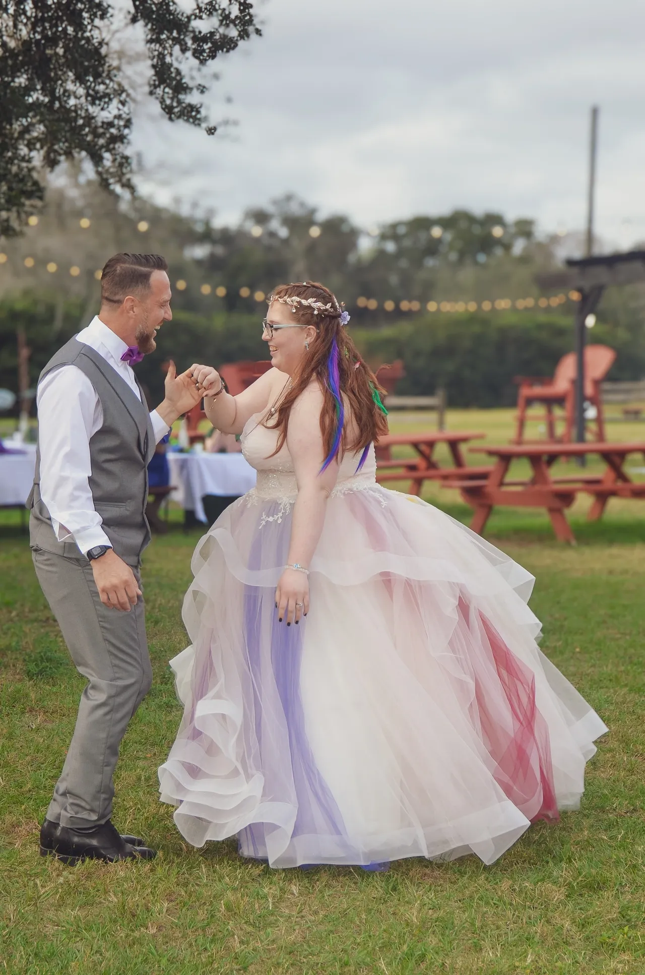 A person in a colorful layered gown and a person in a gray vest dancing together on grass at an outdoor event.