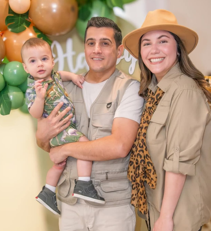 A family dressed in safari-themed clothing poses in front of a balloon arch for a celebration.