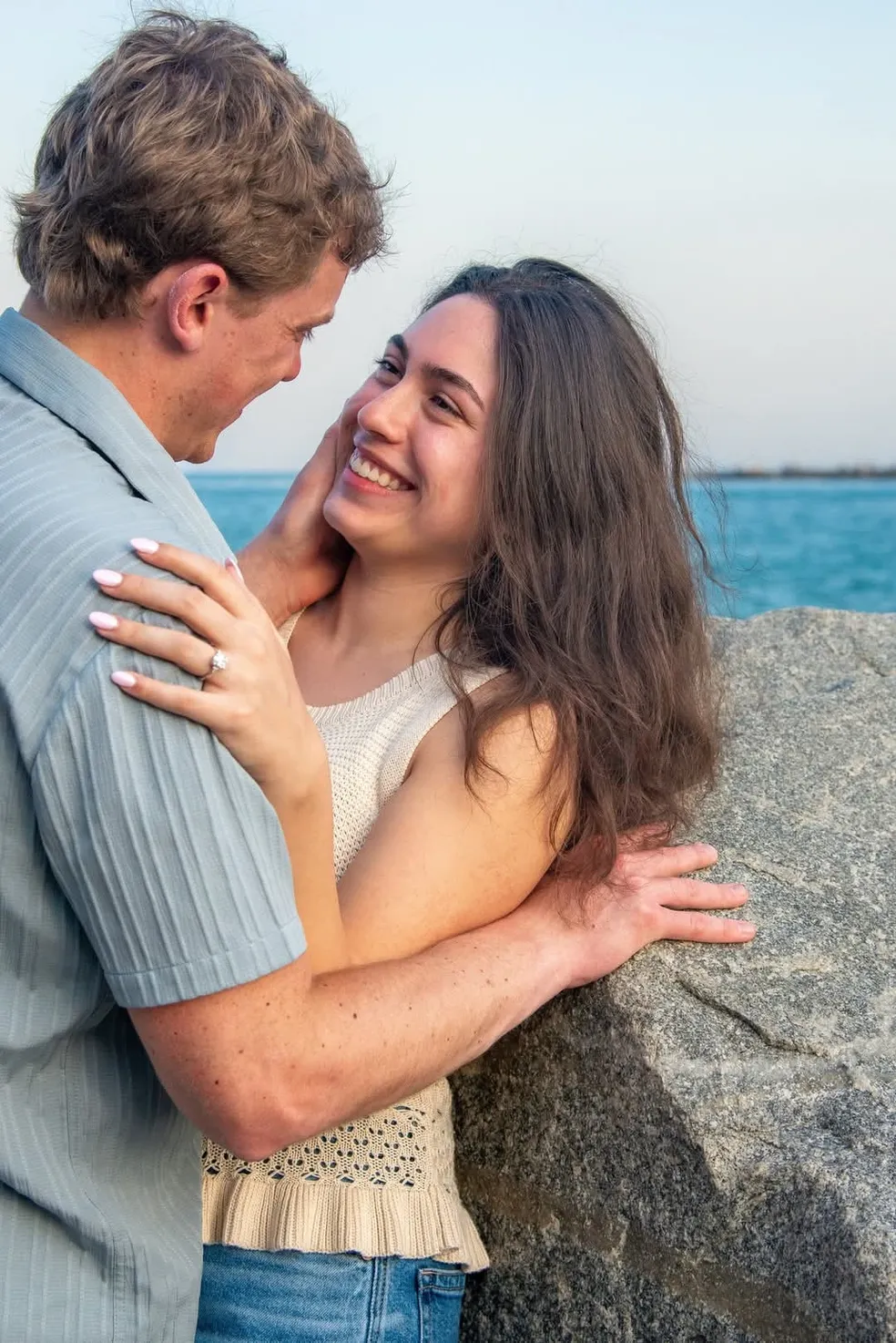 A couple embracing and smiling at each other by a rocky shore overlooking the ocean.