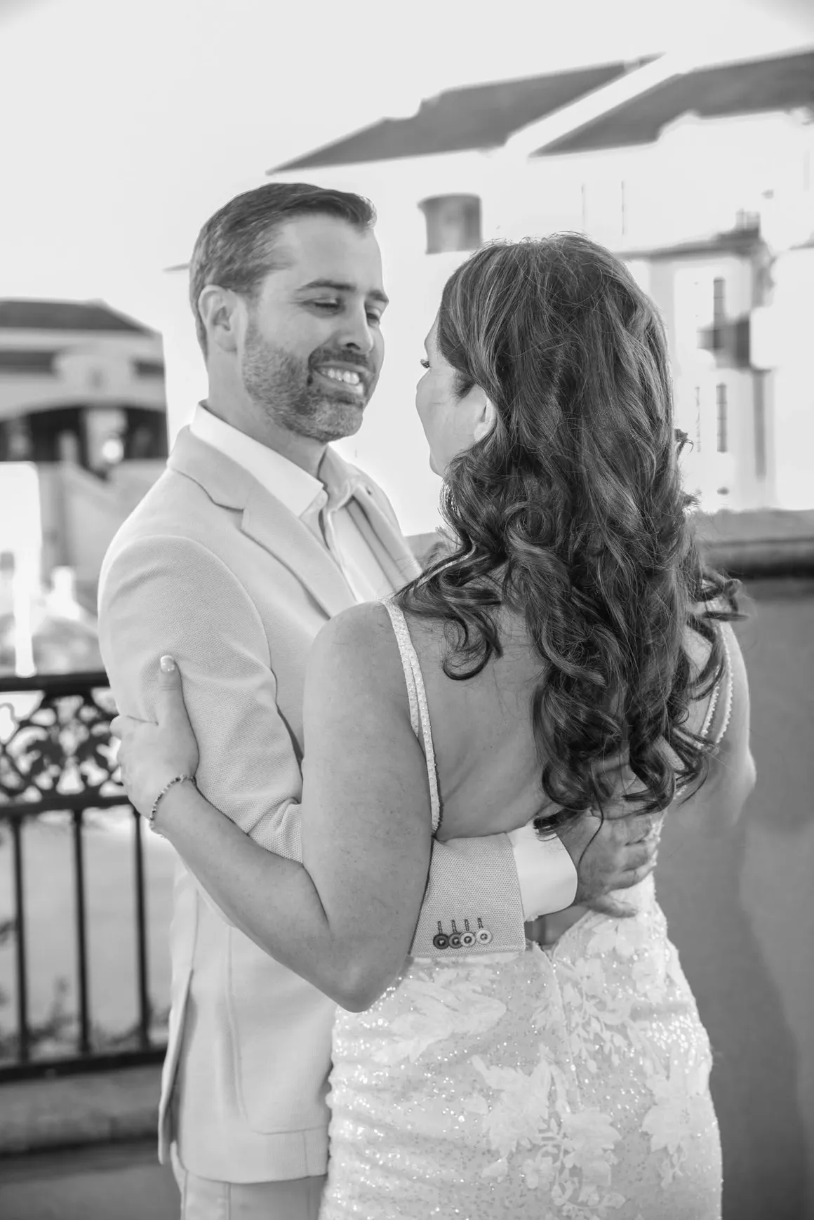 A couple in wedding attire embracing and looking at each other outdoors, captured in black and white.