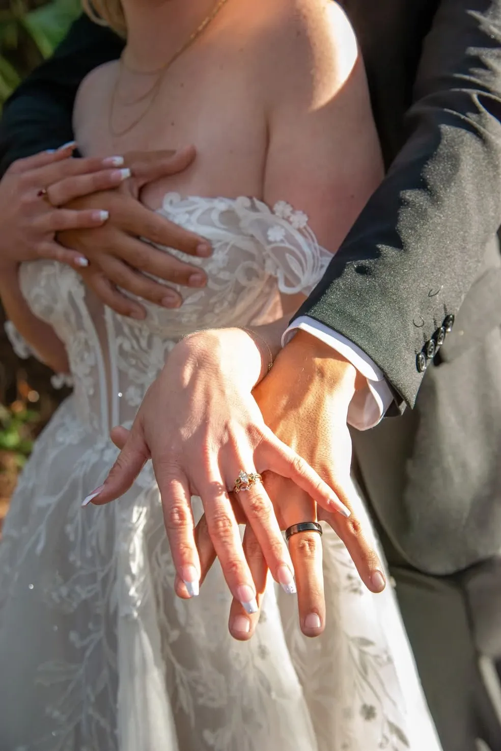Close-up of a couple showcasing their wedding rings on their hands, with the bride wearing a white lace gown.