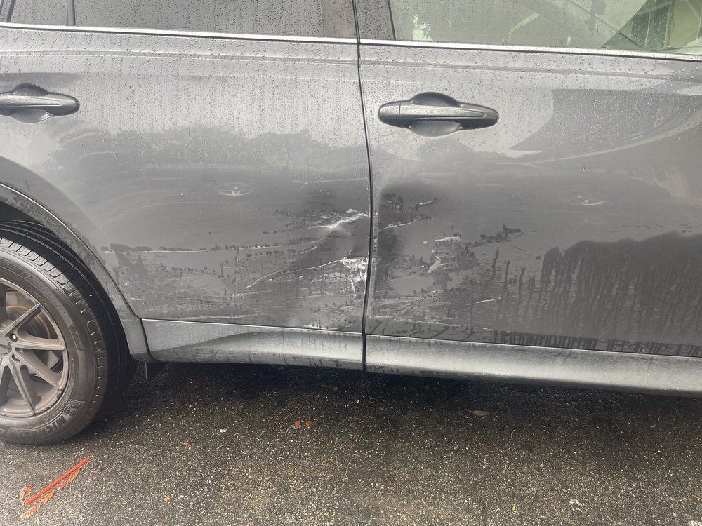 A gray car with a damaged door is parked on the side of the road.