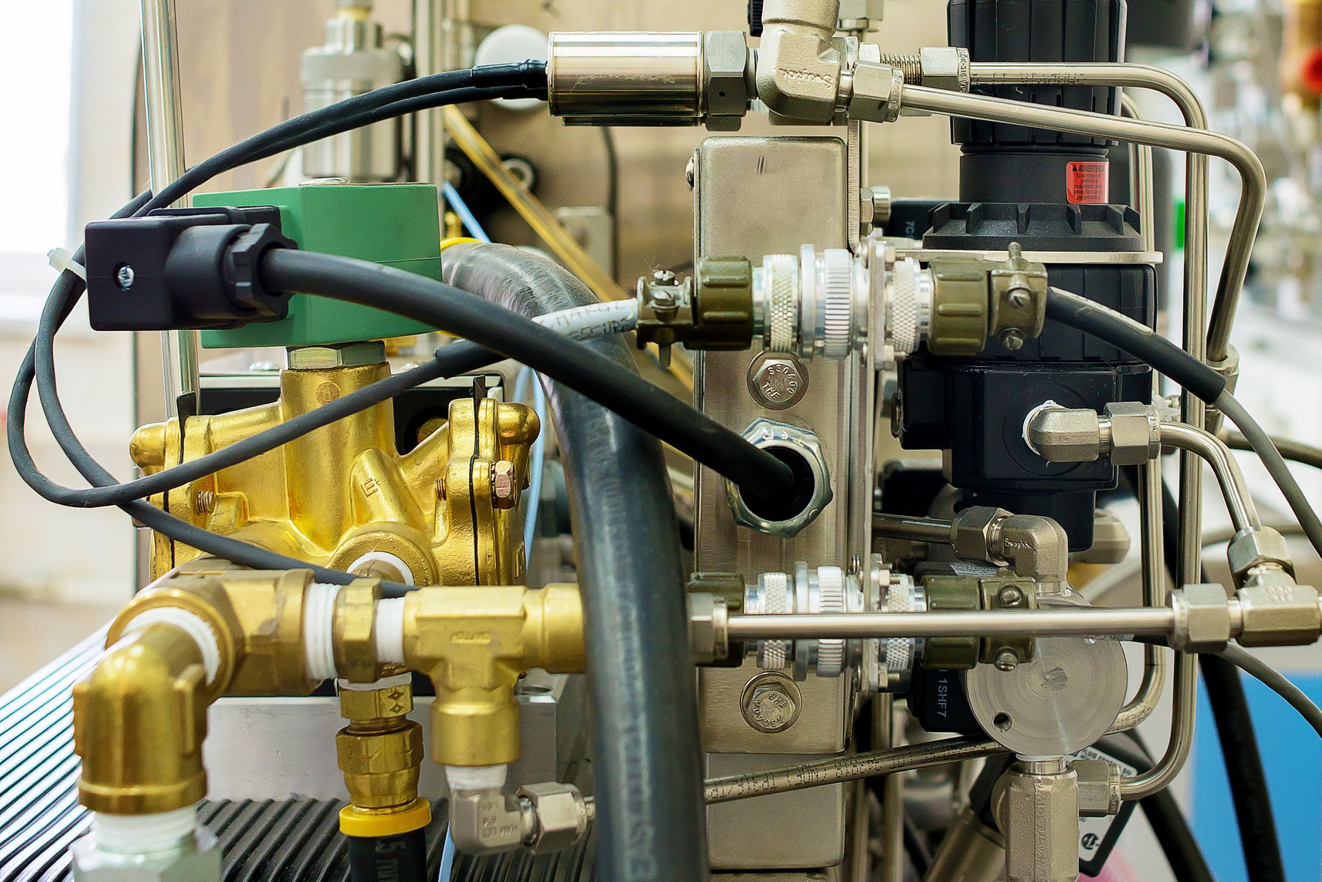 Detalhe de uma máquina industrial com válvulas, tubos e cabos de latão em uma estrutura metálica.