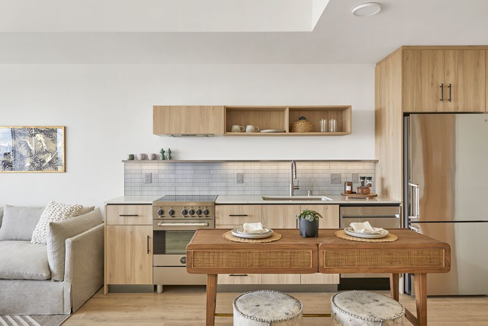 Bright modern kitchen and dining area with wood cabinetry, stainless appliances, and a table set for two