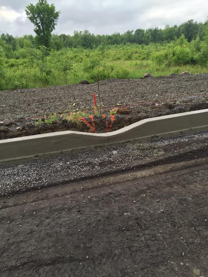 Un mur de béton est en cours de construction au bord d’un chemin de terre.