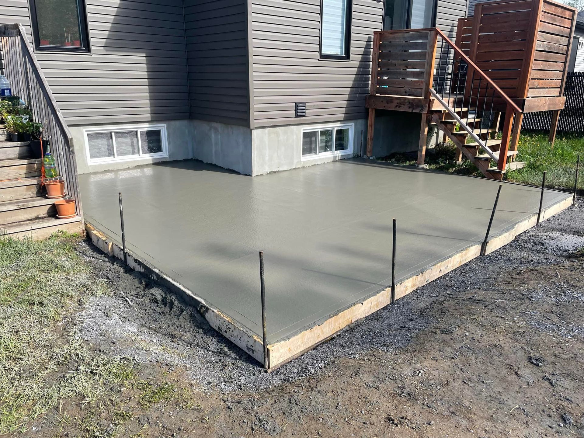 Une terrasse en béton est en cours de construction devant une maison avec des escaliers.