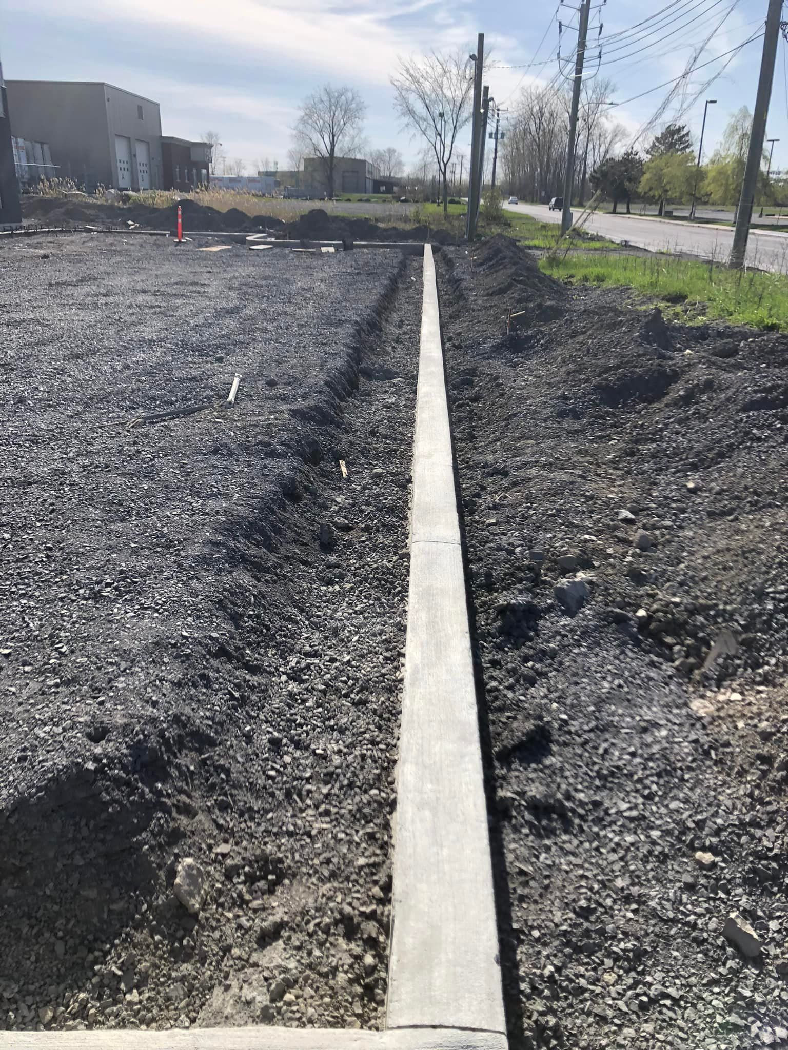 Une bordure en béton est en cours d'installation au bord d'un chemin de gravier.