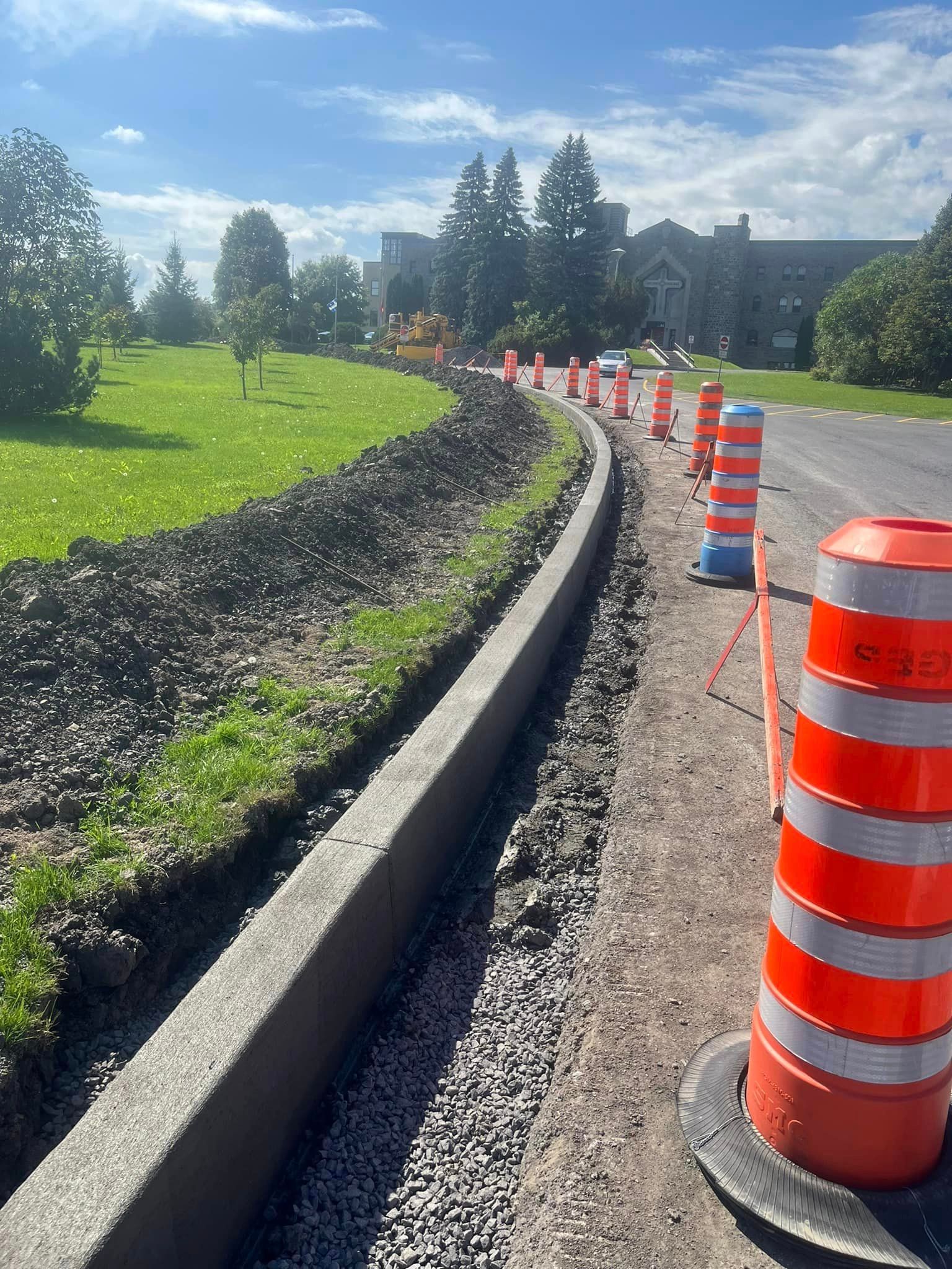 Une rangée de cônes de signalisation orange et blancs se trouve sur le bord d’une route.