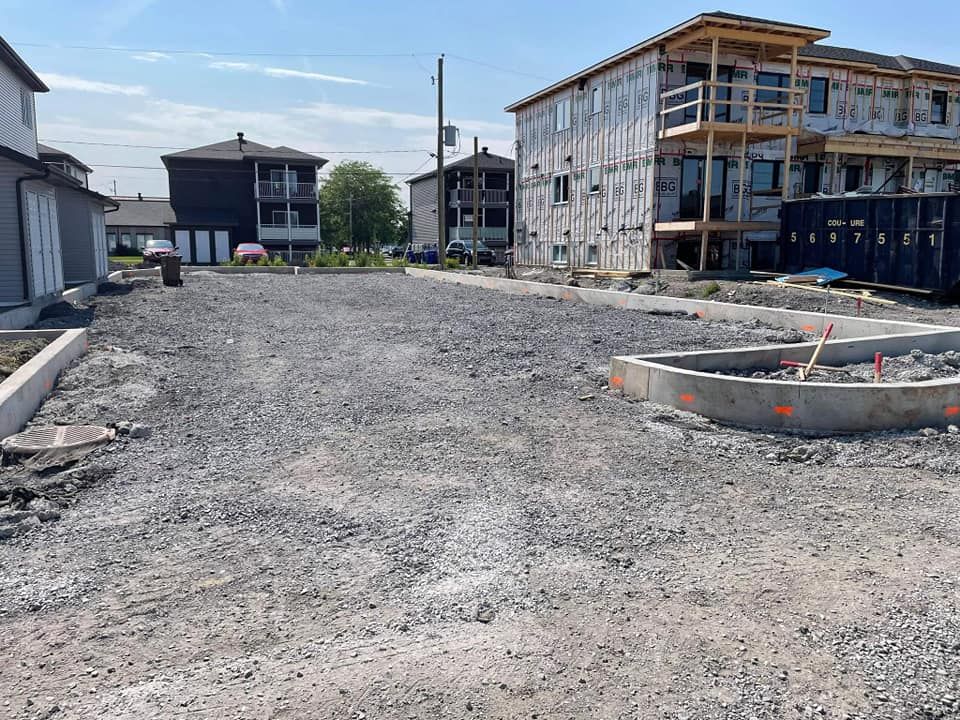 Un chantier de construction avec beaucoup de gravier et des bâtiments en arrière-plan.