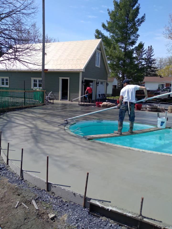 Un homme coule du béton dans une piscine devant une maison.