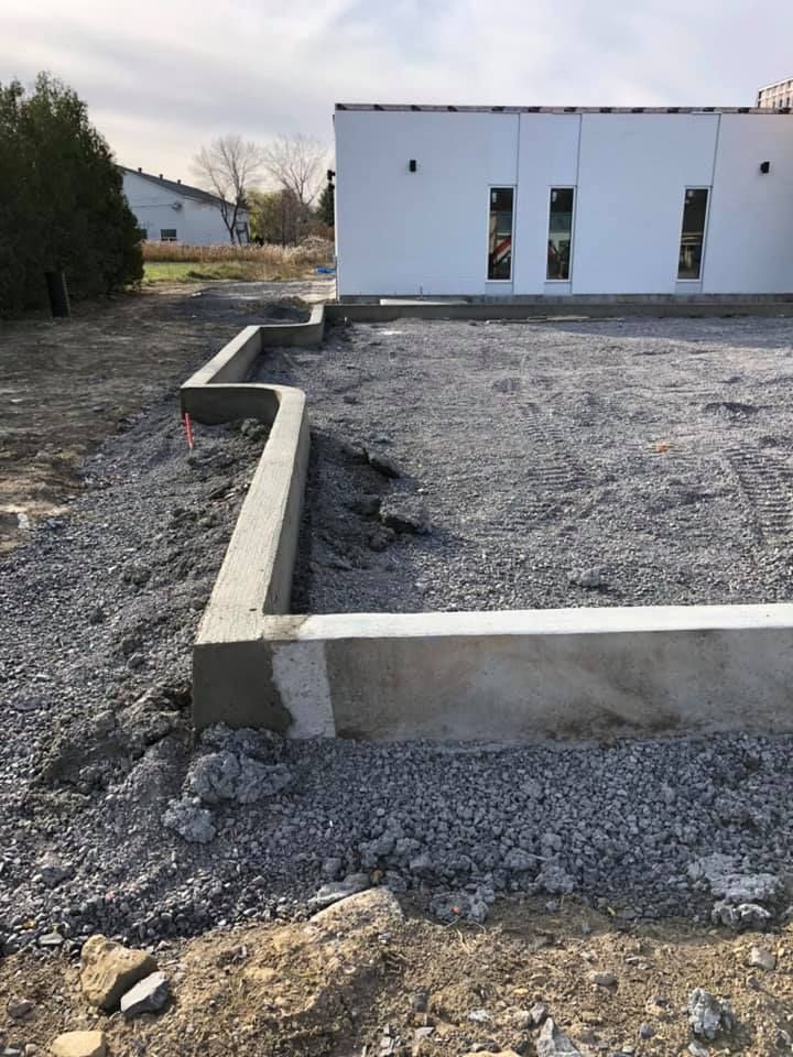 Un bâtiment blanc est en construction au milieu d’un champ de terre.