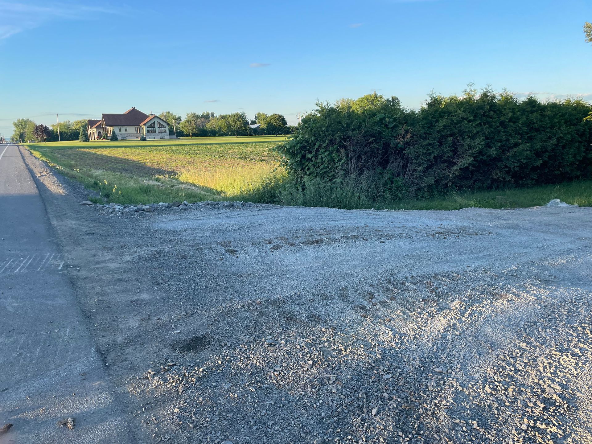 Une route de gravier traversant un champ avec une maison en arrière-plan.