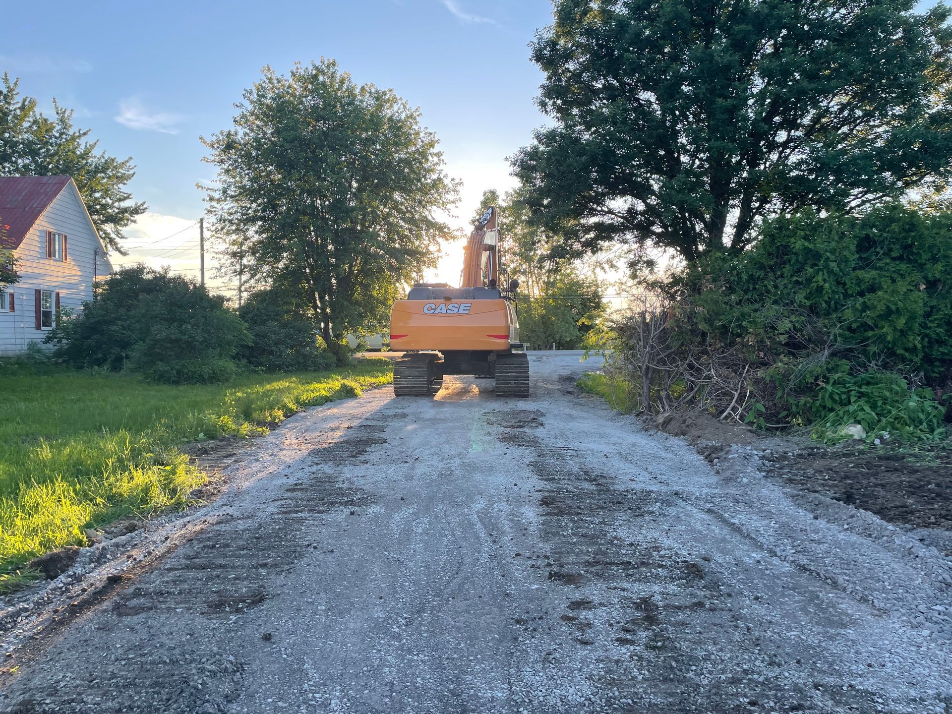 Une grande excavatrice orange roule sur un chemin de terre.