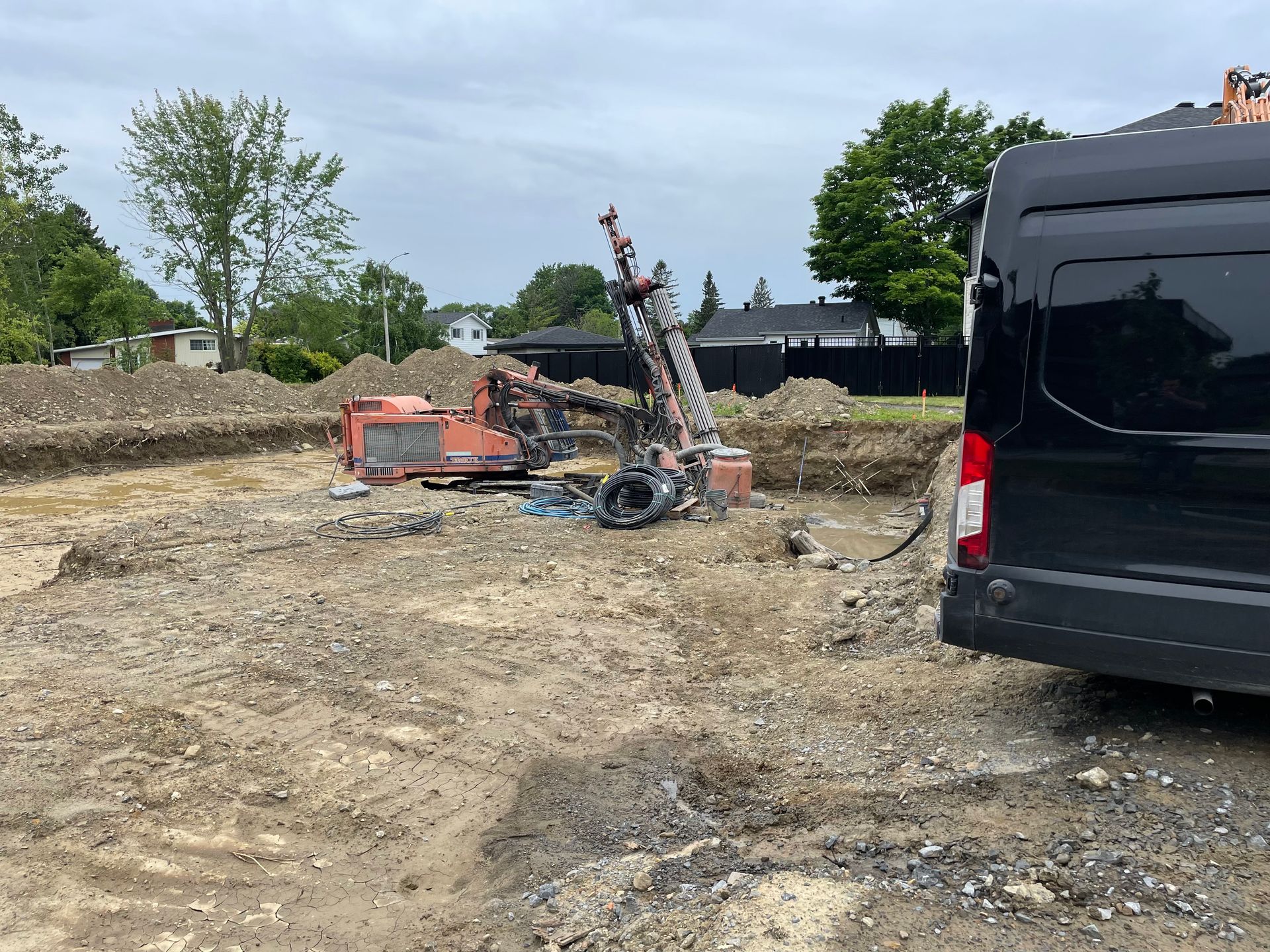 Une camionnette noire est garée dans un champ de terre à côté d'un chantier de construction.