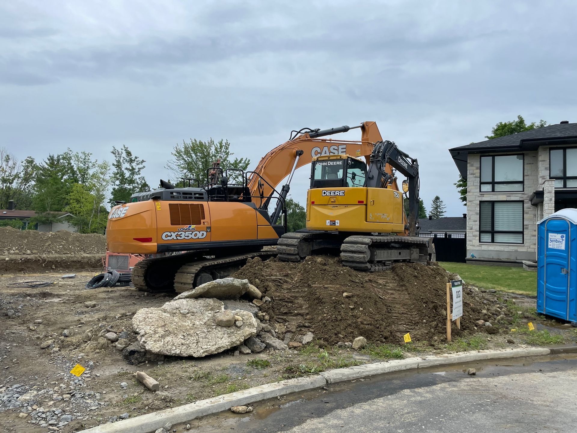 Une grande excavatrice travaille sur un chantier de construction devant une maison.