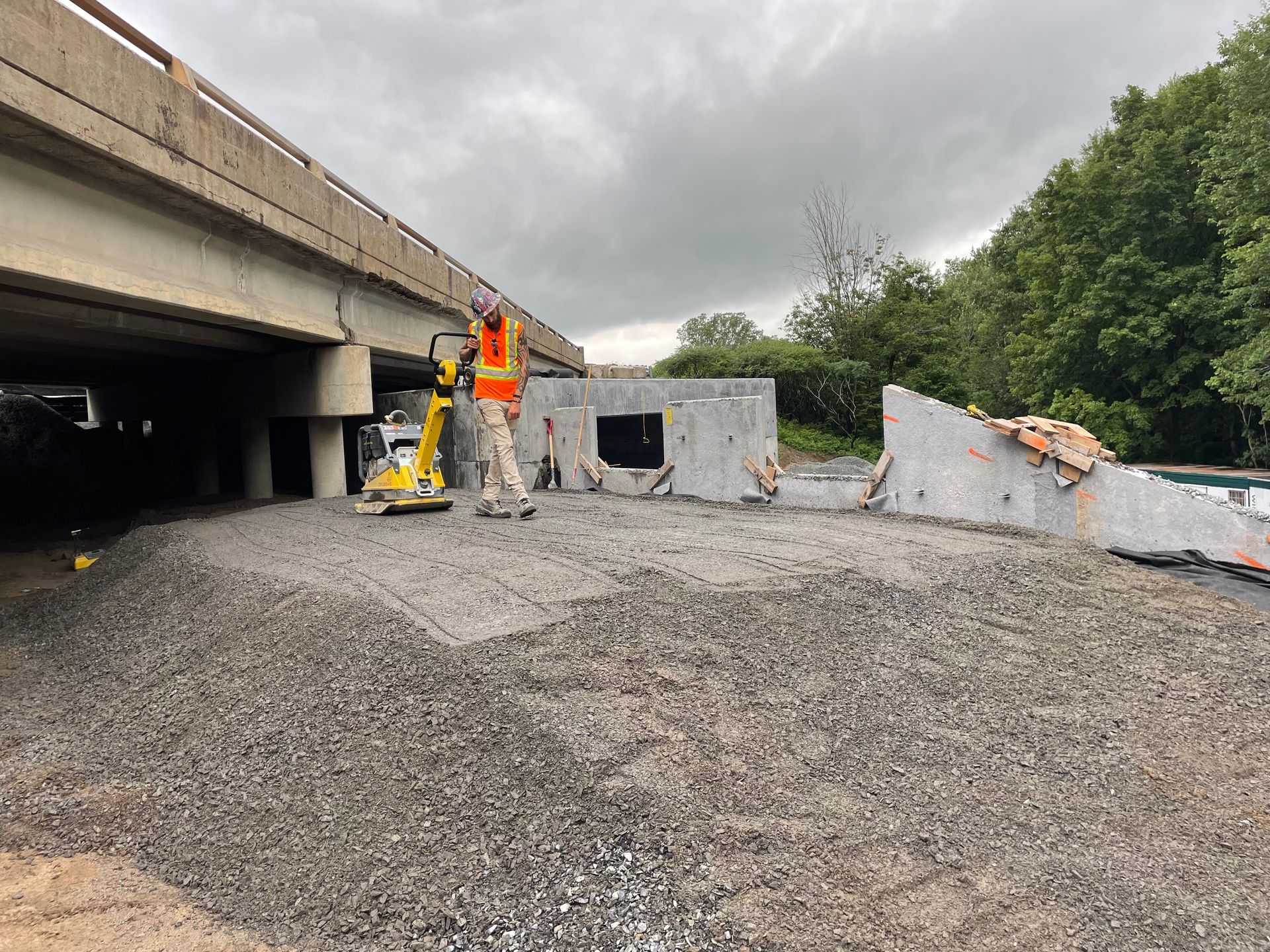 Un ouvrier du bâtiment se tient sur une route de gravier sous un pont.