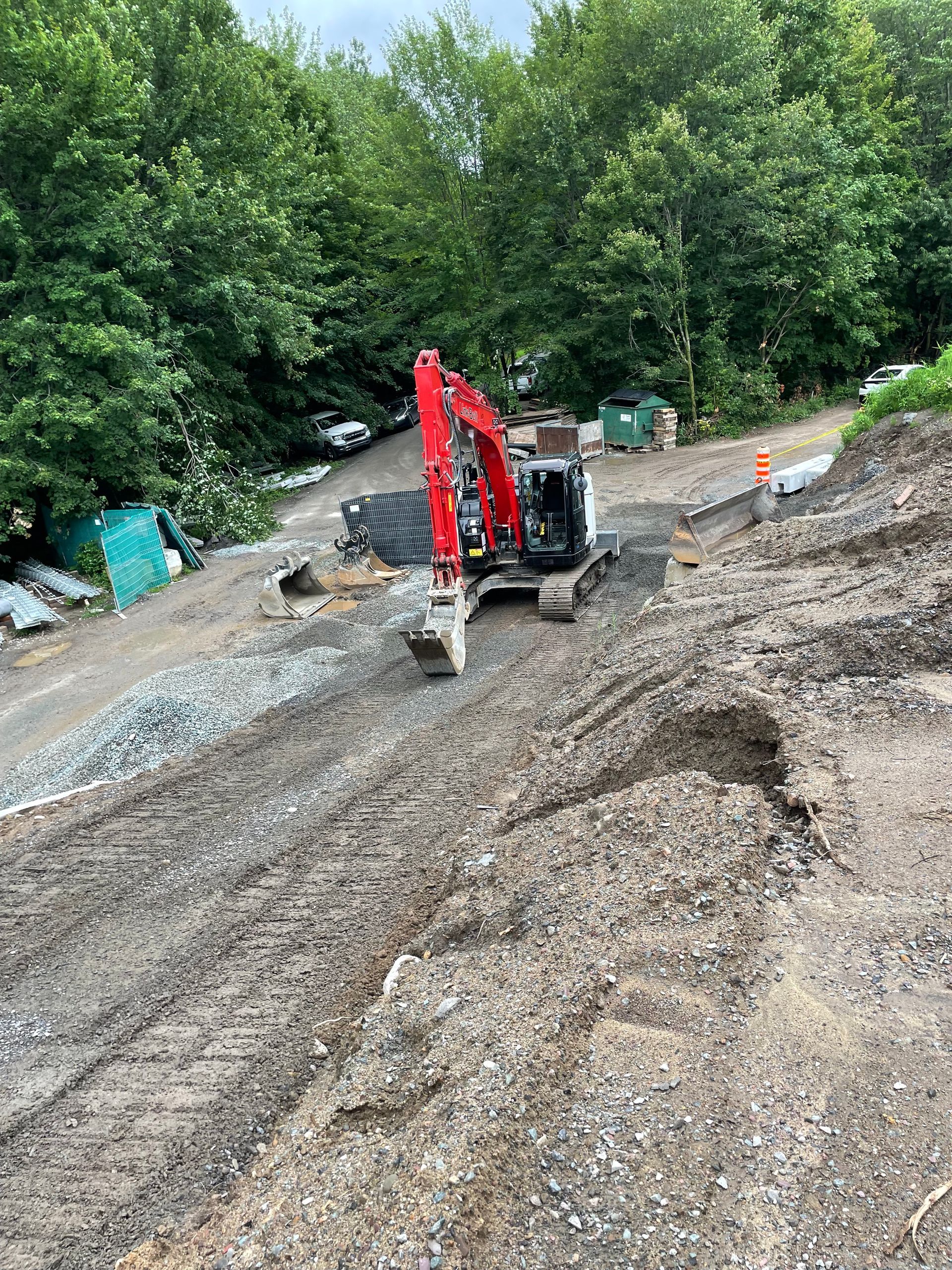 Une excavatrice rouge est assise au sommet d’une colline de terre.