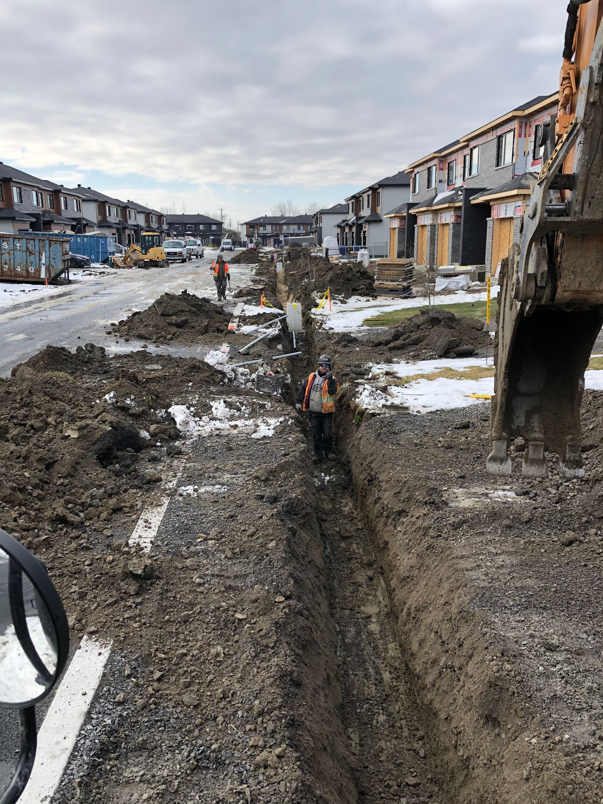 Une grosse pelle creuse une tranchée au milieu d’une rue.