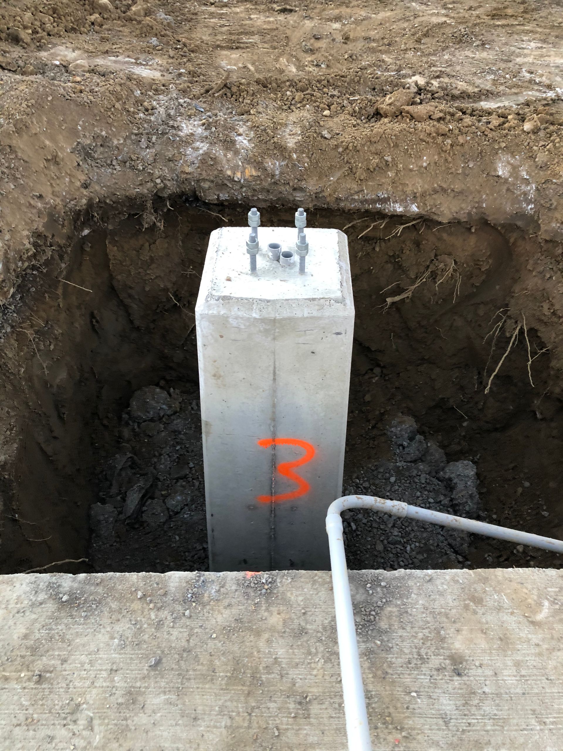 Un poteau en béton sur lequel est peint le numéro 3 se trouve dans un trou dans le sol.