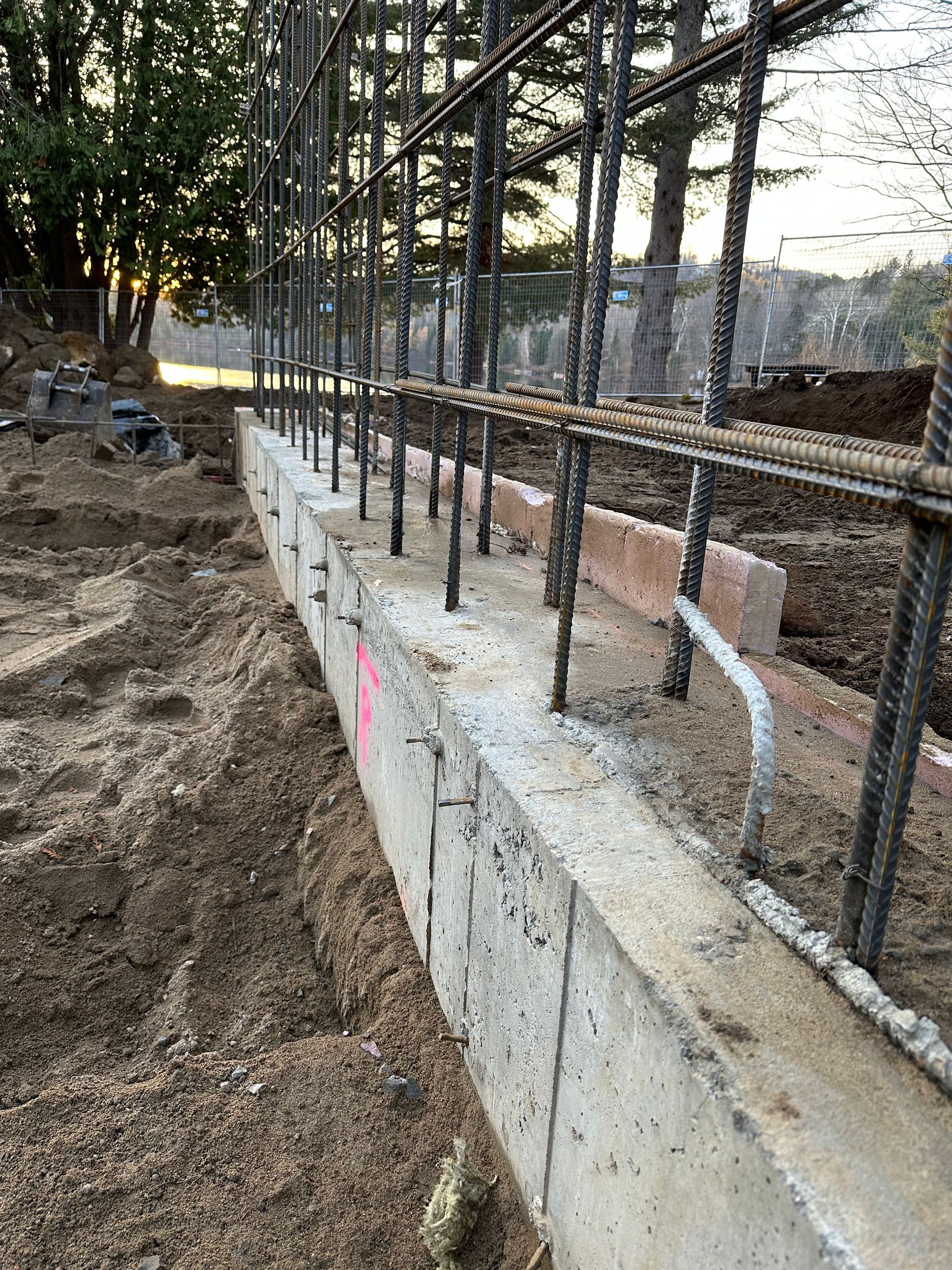 Un mur de béton est en cours de construction, entouré d'une clôture métallique.