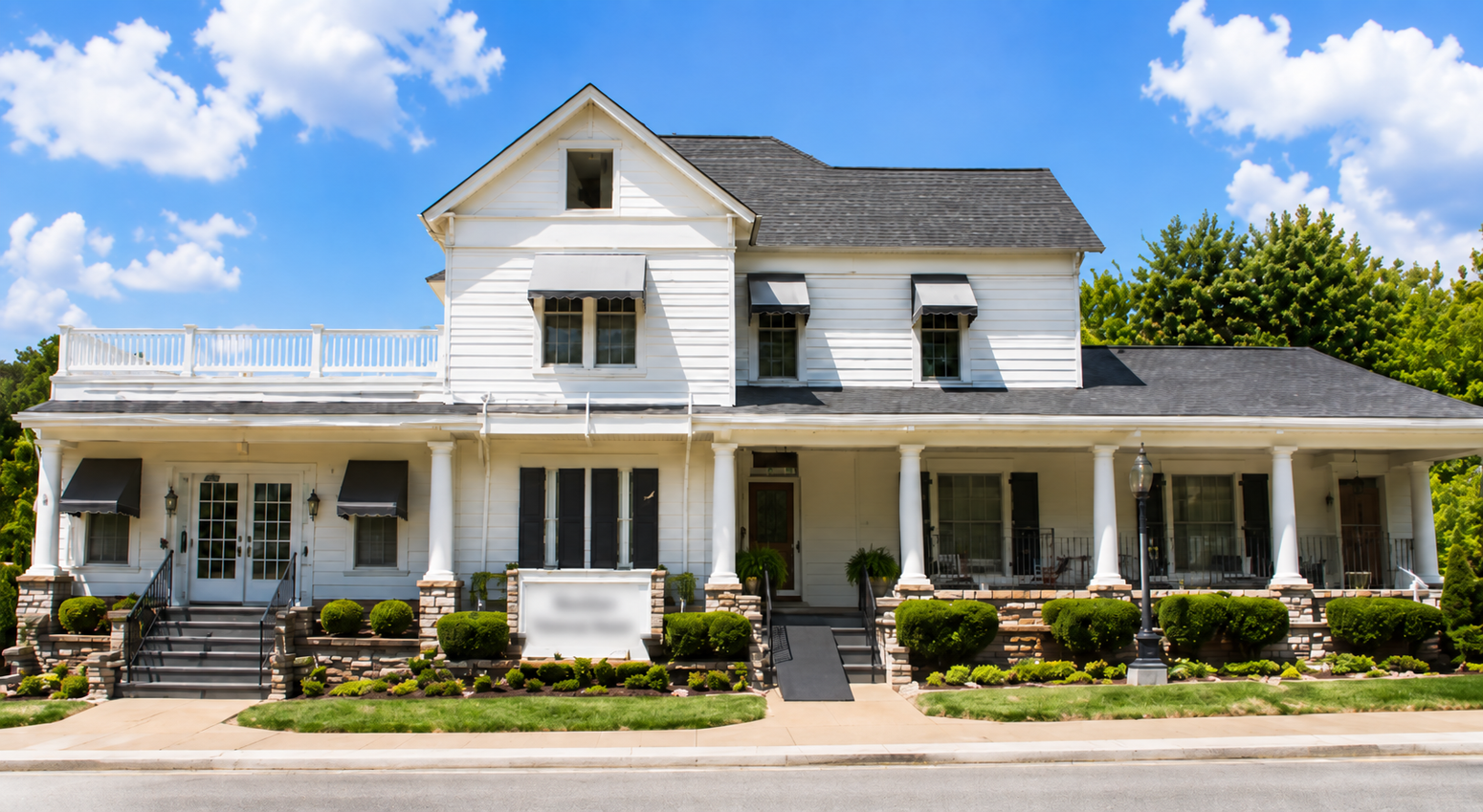 White two-story house with a covered porch, dormer windows, and a manicured front garden under a blue sky