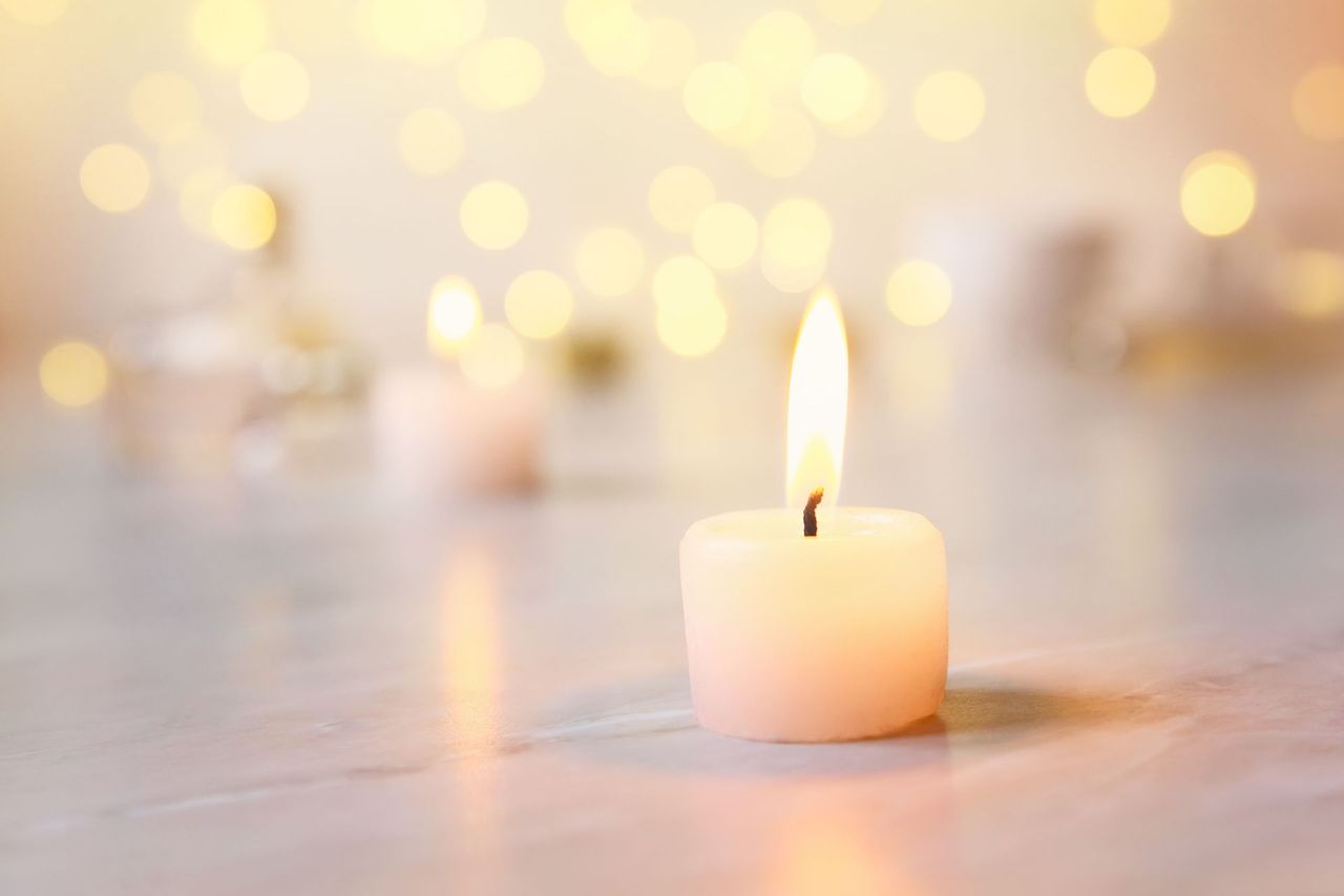 Lit white tealight candle on a soft, warm bokeh background