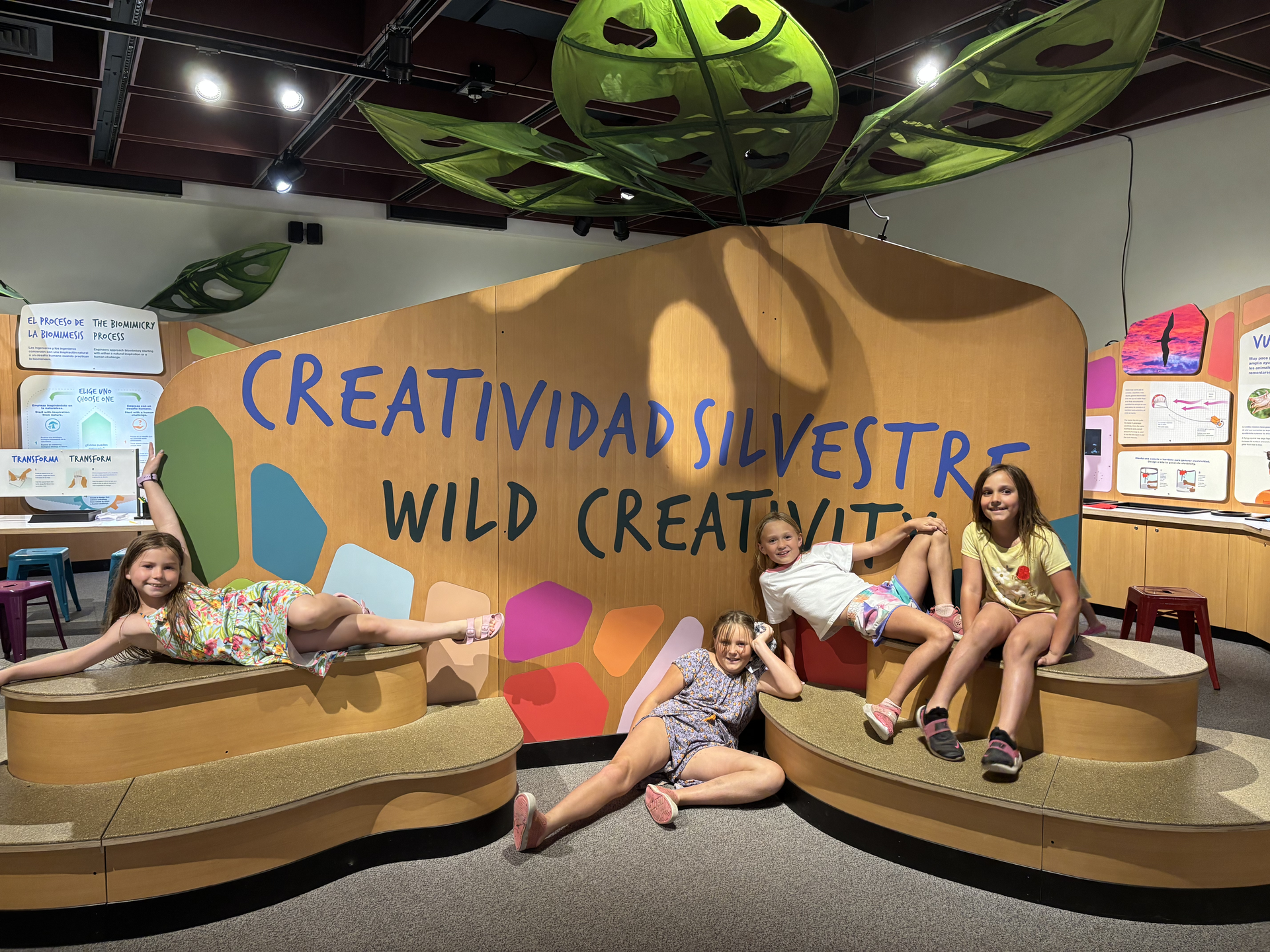 Children posing on cardboard animal props in a creative exhibit with “Creatividad Silvestre / Wild Creativity” backdrop