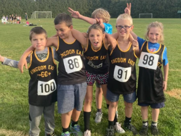 Five KESD children in black and yellow uniforms posing on a grassy field