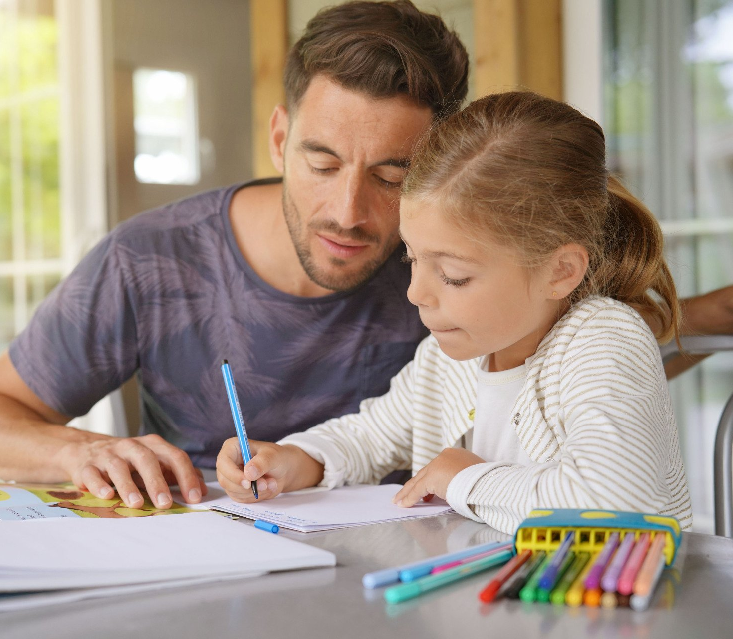 Father sitting  at a table with daughter who is writing