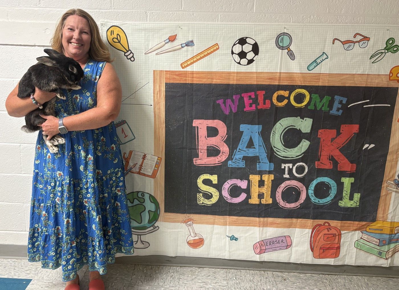 Principal, Tammy MacQueen holding school rabbit in front of Welcome Back to School sign.