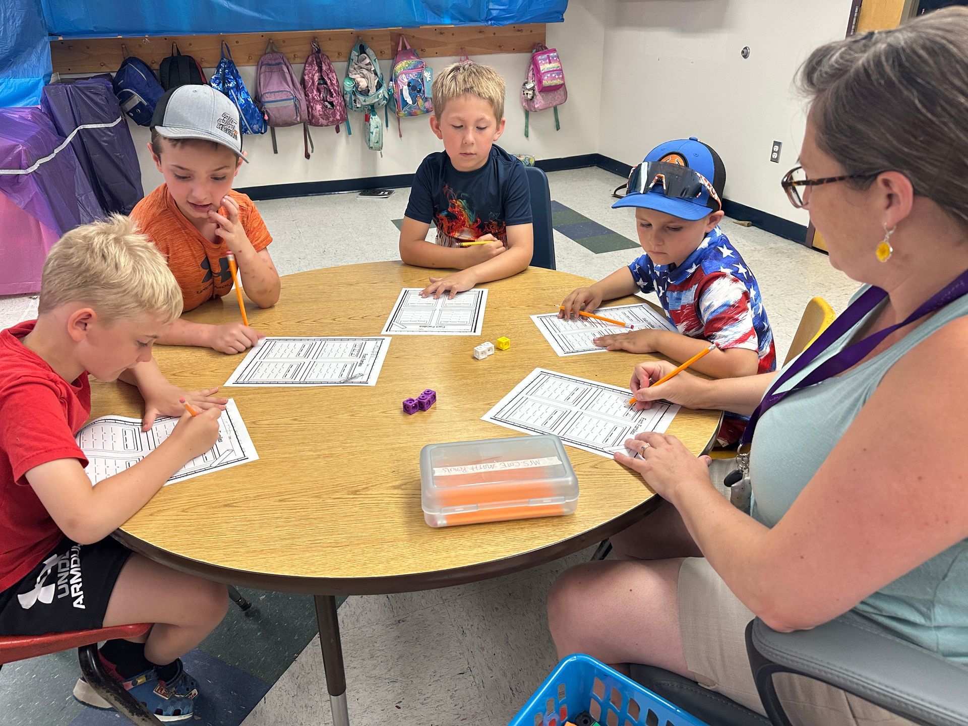 Adults and children seated around a table, working on papers in a classroom setting