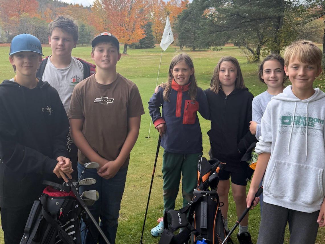 group of Newark students with golf clubs and bags standing outdoors in autumn.