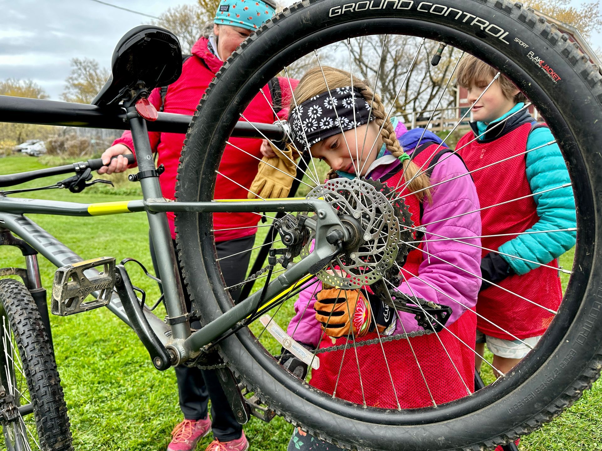 Children fix a bicycle wheel together on a grassy field.