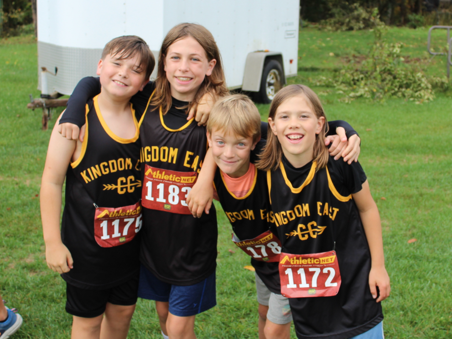 Four children in black and yellow race shirts posing together on a grassy field