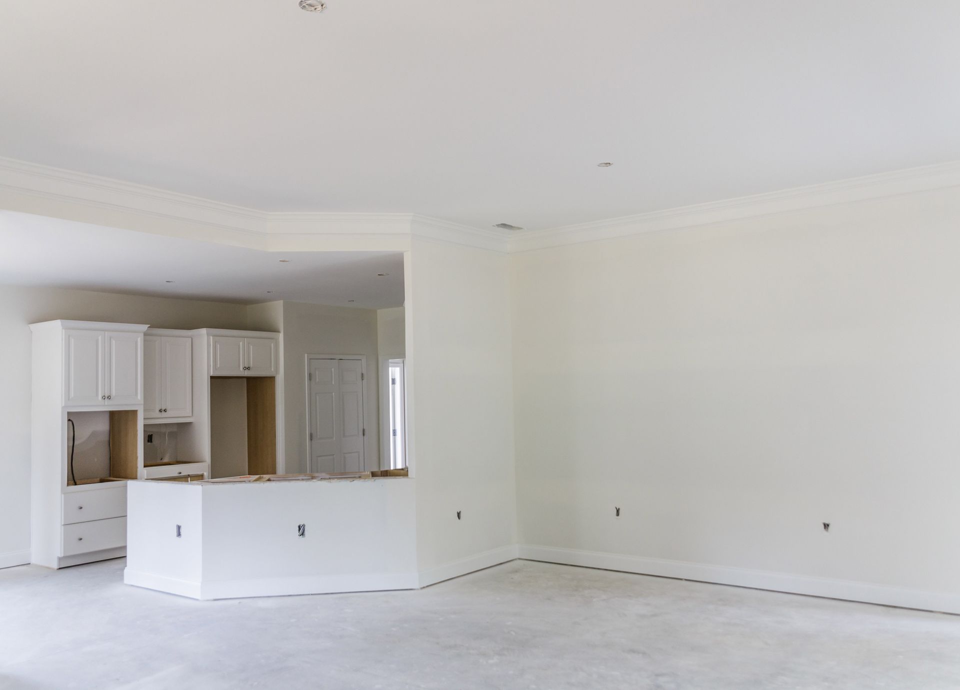 Empty white living room with open kitchen and light-colored flooring